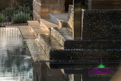 Custom black pebble stone water feature into pool.
