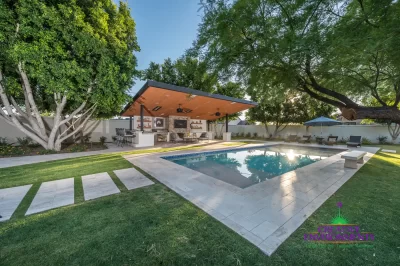 Custom backyard design with natural stone decking, blue traditional pool and angled shade structure.